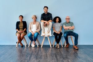 Full length shot of a diverse group of businesspeople sitting down and waiting in line against a blue background